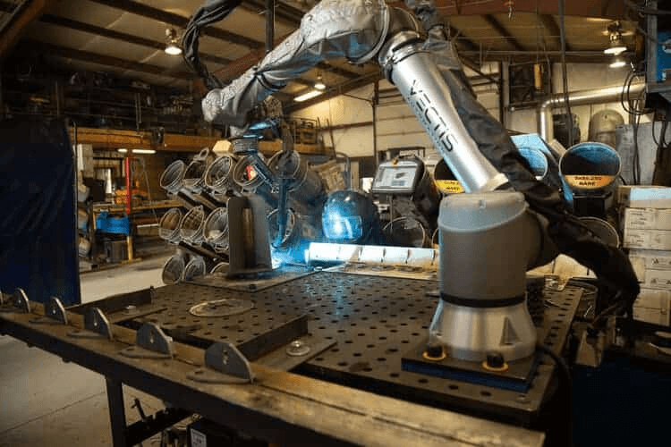 Technician using a dry-ice blaster to remove slag from a robot wrist and torch